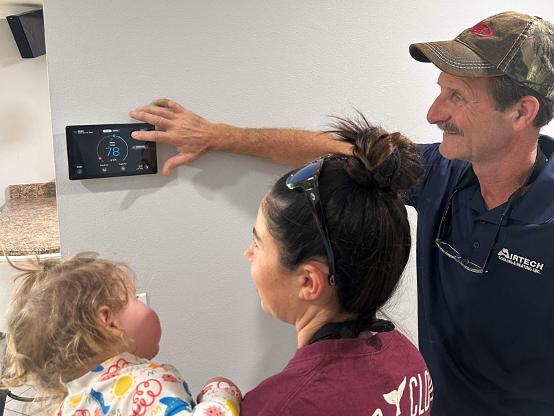 Technician turning on thermostat with children watching